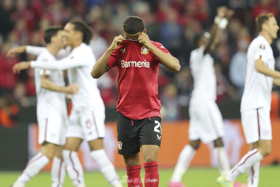 勒沃库森边锋迪亚比带球疾驰如风，试图突破罗马两名防守球员的左右夹击，三人身影在灯光下拉出长长的轨迹。