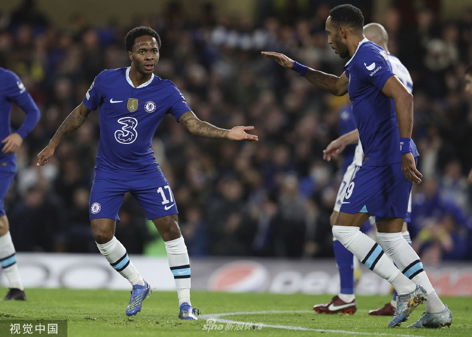 斯特林破门后张开双臂滑跪庆祝，背景是陷入沸腾的蓝色看台和激动飞奔而来的队友