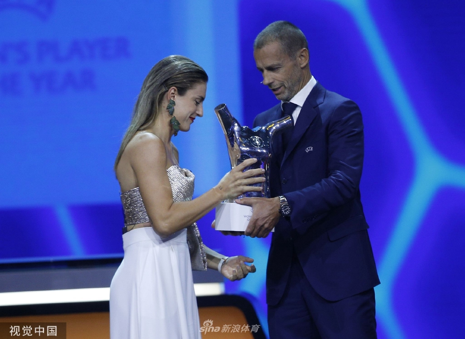普特拉斯在领奖台上高举奖杯，向全场致意，红色礼服衬托出其自信与王者气场