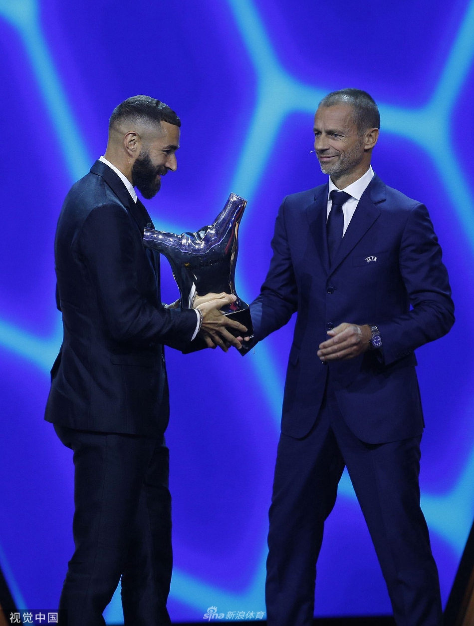 本泽马身着优雅西装，在领奖台上深情亲吻晶莹剔透的欧足联最佳球员奖杯，聚光灯下奖杯与他的专注神情交相辉映