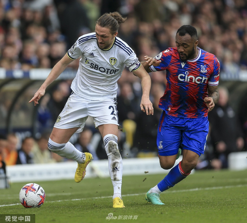 水晶宫前锋马特塔进球后张开双臂，在利兹联禁区内激情滑跪庆祝，身后是沮丧的主队后卫