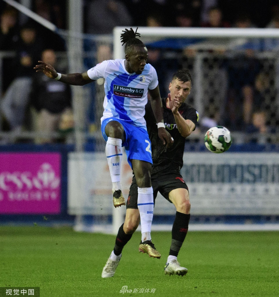 一位年轻的小球迷身披巴罗队围巾，在看台上专注地凝视赛场，眼神中充满了对足球最纯粹的热爱。