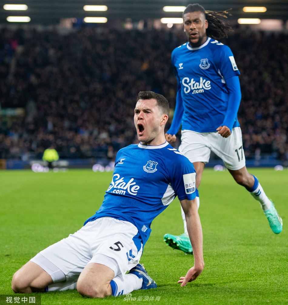 哈里·凯恩主罚点球瞬间，他冷静施射，埃弗顿门将奋力扑救但未能触及皮球，身后是表情各异的双方球员。