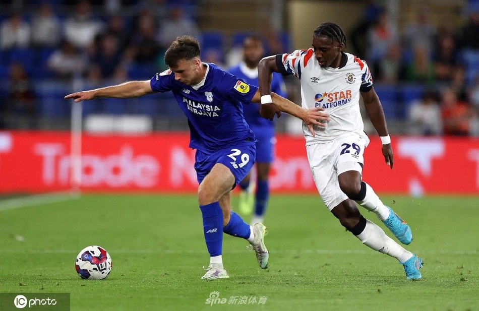 卢顿队进球功臣张开双臂，在卡迪夫城球场内激情滑跪庆祝，身后是沮丧的主队后卫。