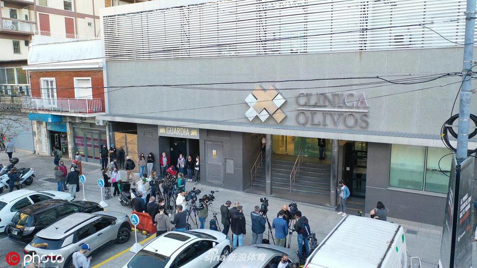 温暖的烛光中，几位女球迷紧紧相拥，脸上挂着泪痕，身后的墙上贴满了为马拉多纳加油的手写标语，画面感人至深。