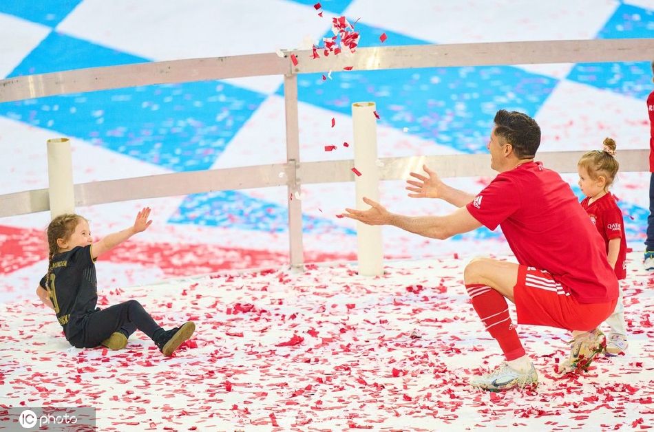 莱万帮助女儿触摸冠军奖盘，孩子小手与银色奖盘形成温馨对比，传承着荣耀与梦想