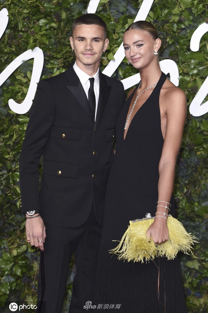 罗密欧身着一袭剪裁利落的黑色军装风格西服，金色纽扣在灯光下熠熠生辉，勾勒出他修长挺拔的身姿，尽显其承袭自父母的时尚基因与贵族气质。