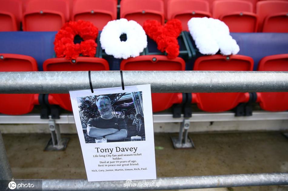 一束以白色为主调的鲜花，被单独放置在一个座位中央，其简洁而庄重的美感，在周围深色座椅的映衬下，无声地诉说着无尽的思念。它像一枚温柔的勋章，别在这位球迷生前最爱的位置上。