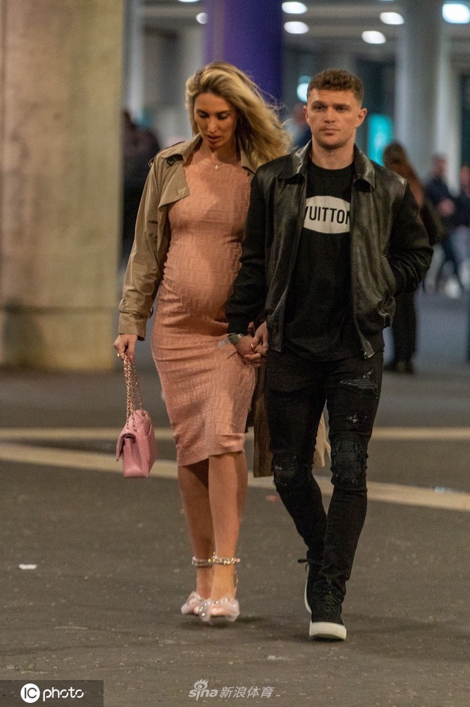 特里皮尔与女友在温布利体育场拳赛现场亲密合影，两人都身着时尚的黑色外套，身后是座无虚席、气氛热烈的观众席。