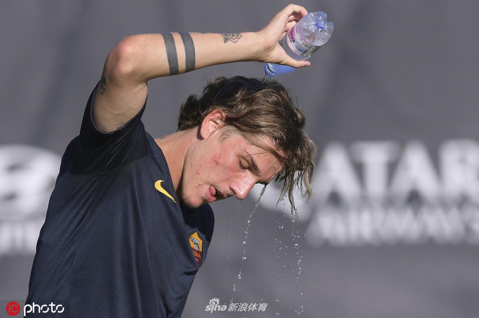 扎尼奥洛双手捧起冰凉的毛巾敷在脑后，表情坚毅，队友们从他身边跑过，背景是罗马训练中心的现代化建筑