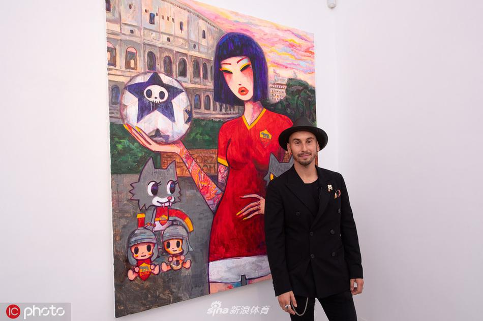 弗洛伦齐与艺术家莱诺在展品前合影，两人笑容灿烂，背景是一组以罗马神话为主题的印花装置，色彩瑰丽，细节丰富。