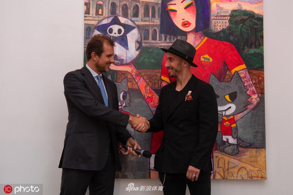 夜幕下的展览现场外景，灯光透过玻璃窗映照出室内的热闹景象，门口伫立着巨大的展览海报，上面是莱诺新系列的罗马元素视觉主图。