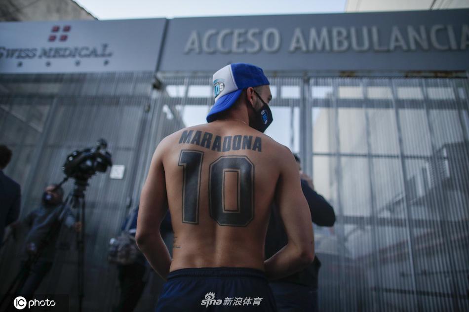 夜色中，一位年迈的球迷身披阿根廷国旗，双手合十放在胸前，眼神中充满了无尽的虔诚与担忧，仿佛在用尽全身力气为心中的英雄祈祷。