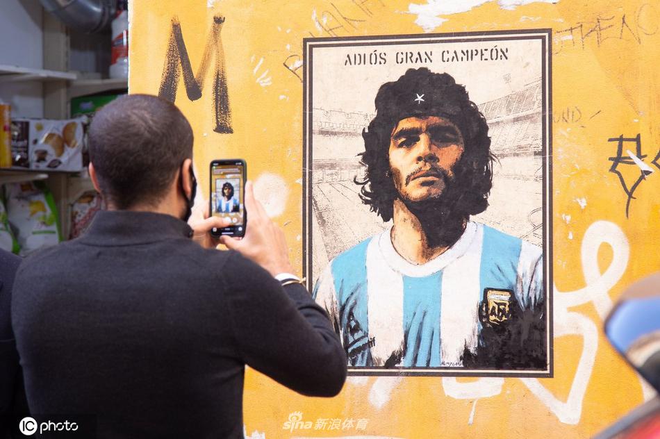 暮色渐浓，一束阳光恰好照亮壁画中马拉多纳的脸庞，仿佛天赐之光，为他镀上一层神圣的光晕，画下的信徒们仰头凝视，久久不愿离去。