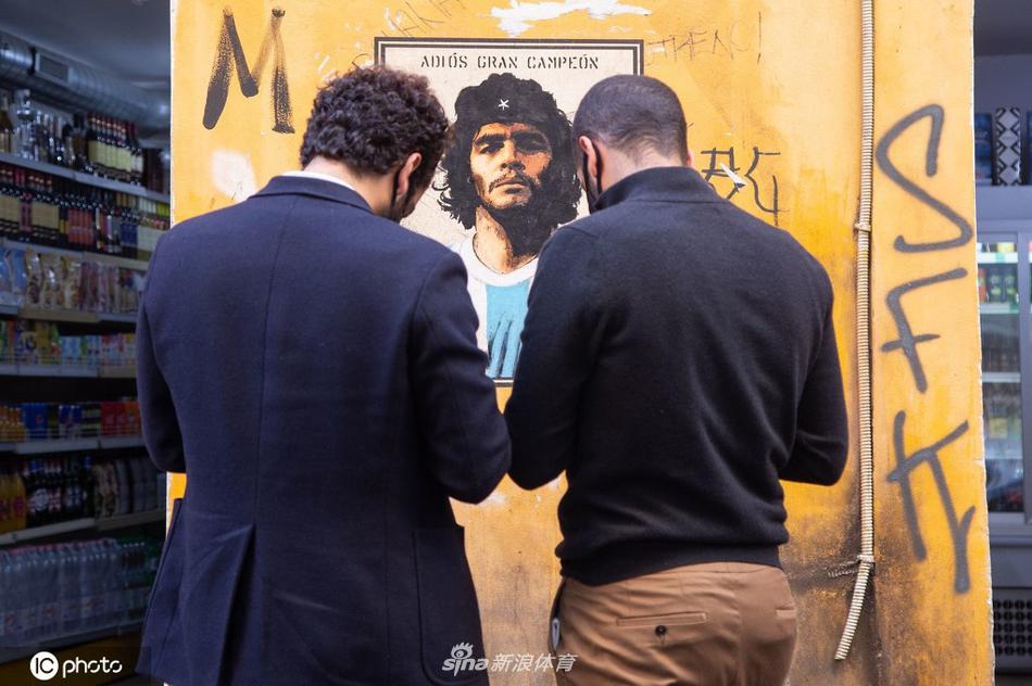 一位身着阿根廷10号球衣的年轻球迷，背对着镜头，与墙上的马拉多纳壁画合影。两件相同的球衣，一虚一实，诉说着跨越时空的传承与追随。