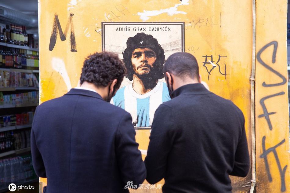 在罗马的街角，一位戴着口罩的球迷静静驻足于崭新的马拉多纳壁画前，举起手机，试图将球王的容颜与此刻的哀思一同定格。