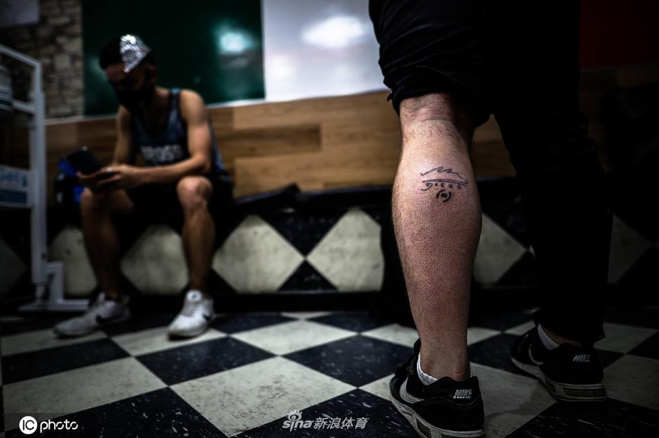 镜头拉近，一位阿根廷球迷的小腿上，一个巨大的马拉多纳经典头像已然成型，深邃的眼神仿佛仍在凝视着他挚爱的绿茵场，黑色的线条在皮肤上显得格外清晰有力。