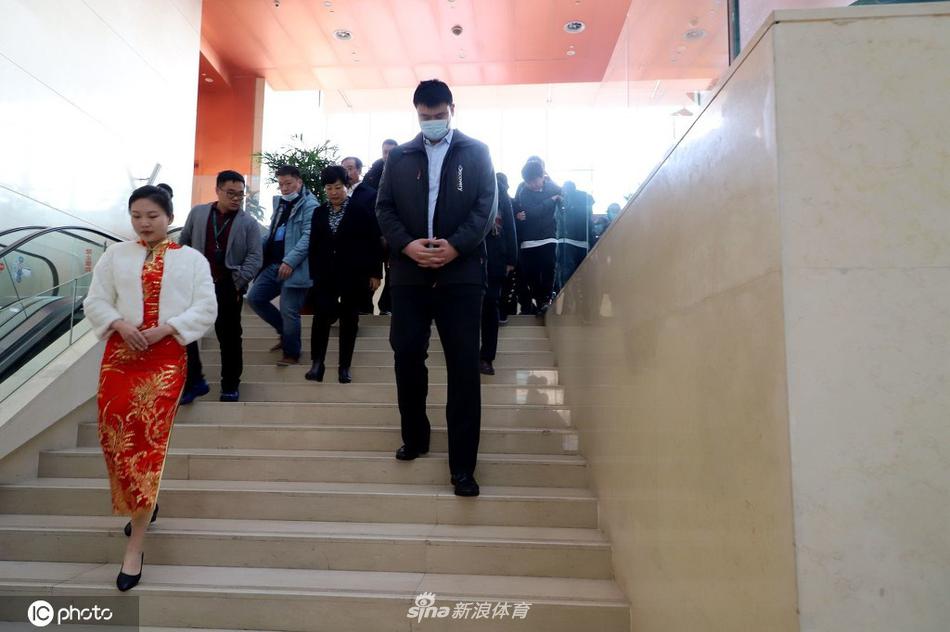 在一张贺龙元帅与篮球队合影的老照片前,姚明与身旁的专家低头细语,探讨着照片背后的革命岁月与体育精神,神情认真而专注。