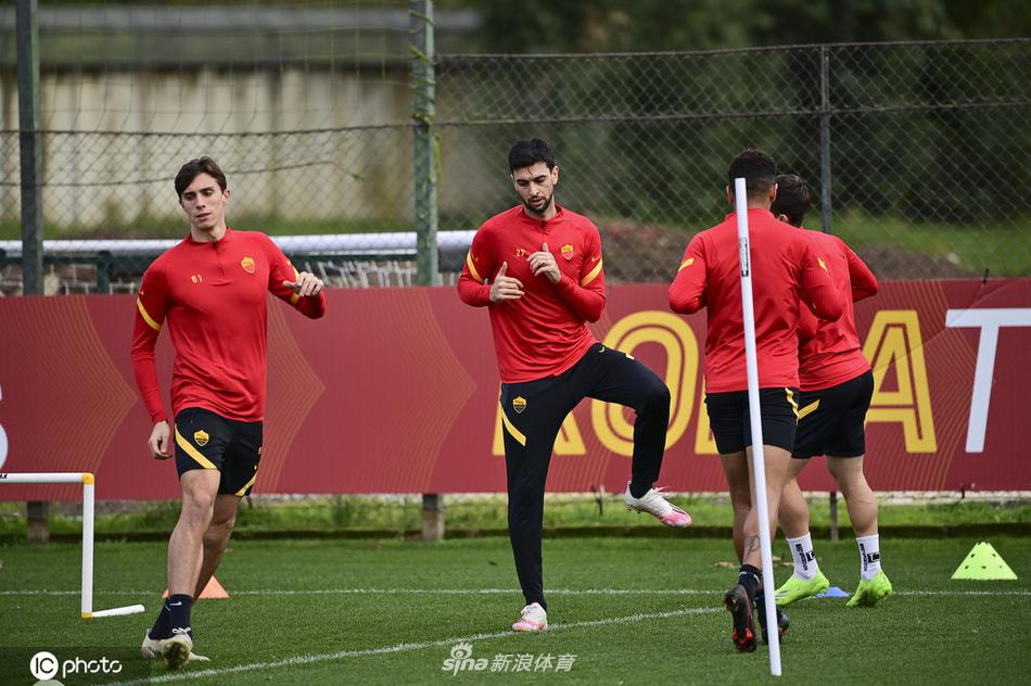 阳光下，罗马球员们正在进行抢圈游戏，一名身着黄色背心的队员试图伸脚断球，而被围在中间的队友则用轻巧的拉球动作试图摆脱，整个画面充满了游戏的快乐和技术的较量。