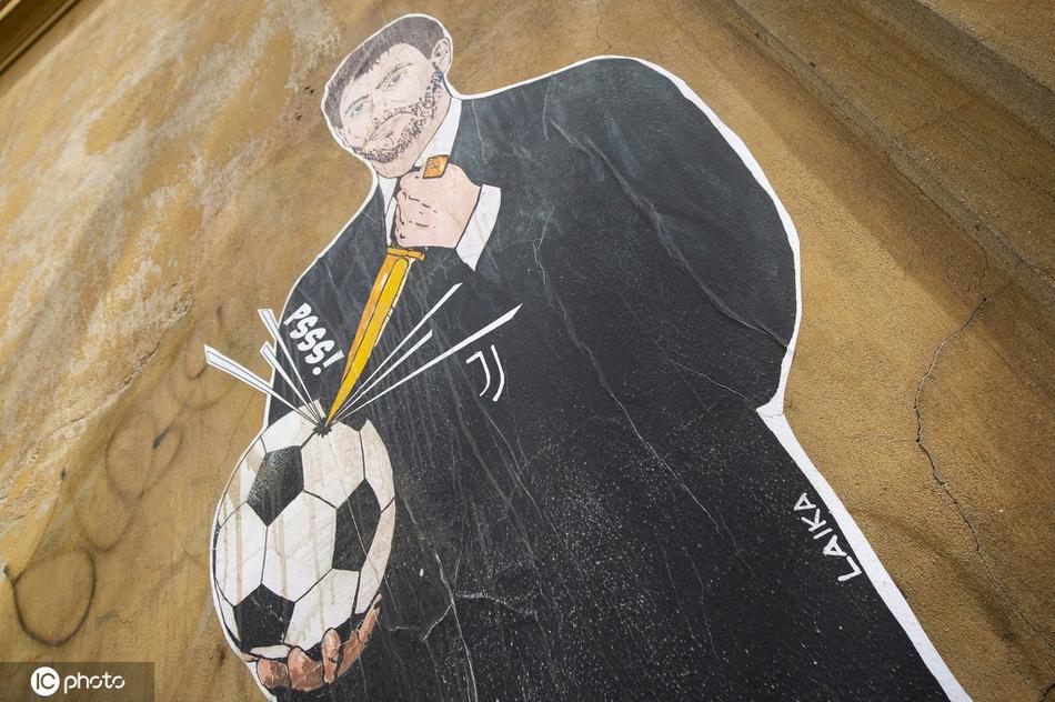 壁画的全景视角下，阿涅利的半身像占据了视觉中心，那只被刺穿的足球仿佛在痛苦呻吟，背景斑驳的墙体与粗糙的街头艺术笔触，让整个抗议场景充满了原始而直接的力量感。