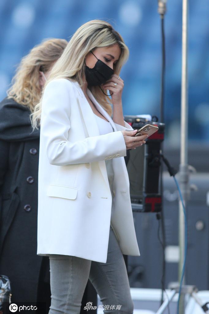 莱奥塔在赛场边专注地看向镜头，低胸设计的白色内搭展现出她傲人的身材曲线，整体造型简约而不失性感。