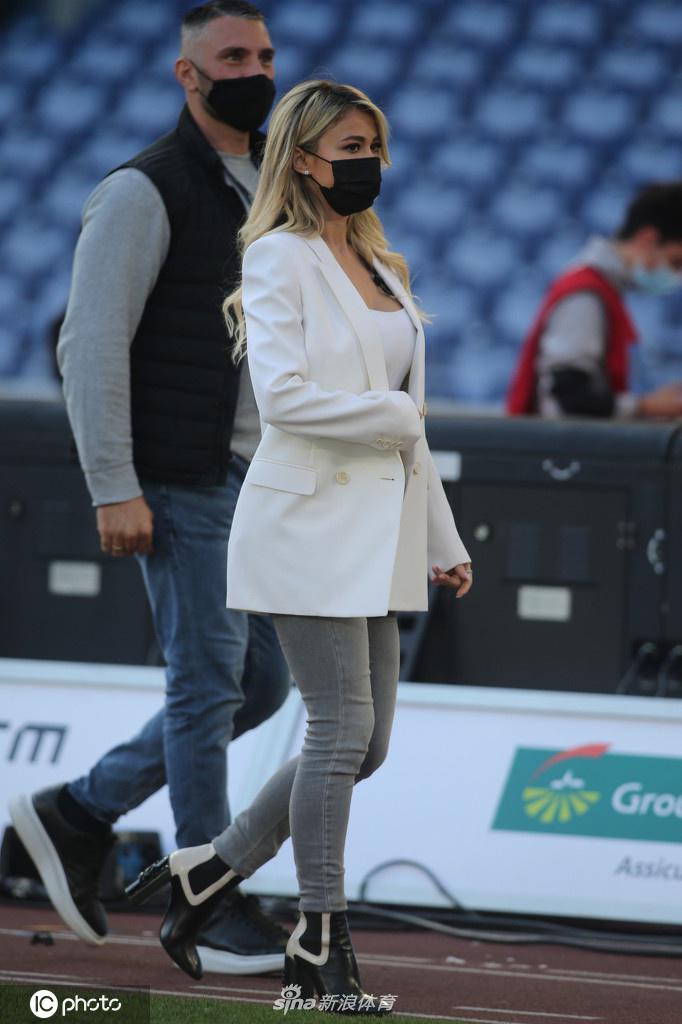 镜头捕捉到莱奥塔低头浅笑的瞬间，白色小西装的干练与低胸背心的柔美在她身上和谐共存，展现出独特的女性魅力。