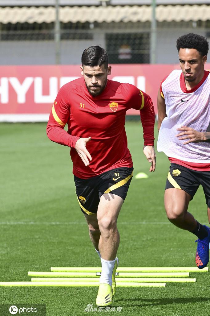 训练场上，两名罗马球员正在进行激烈的抢圈对抗。皮球在两人脚下来回穿梭，扬起细微的草屑。其中一名球员的球衣被汗水浸透，紧贴在身上，折射出训练的严酷。