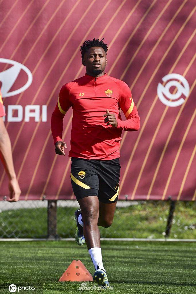 一名罗马球员独自加练射门，他目光如炬，瞄准球门死角，身后的球网在阳光下投下斑驳的影子，整个场景充满了专注和决心。