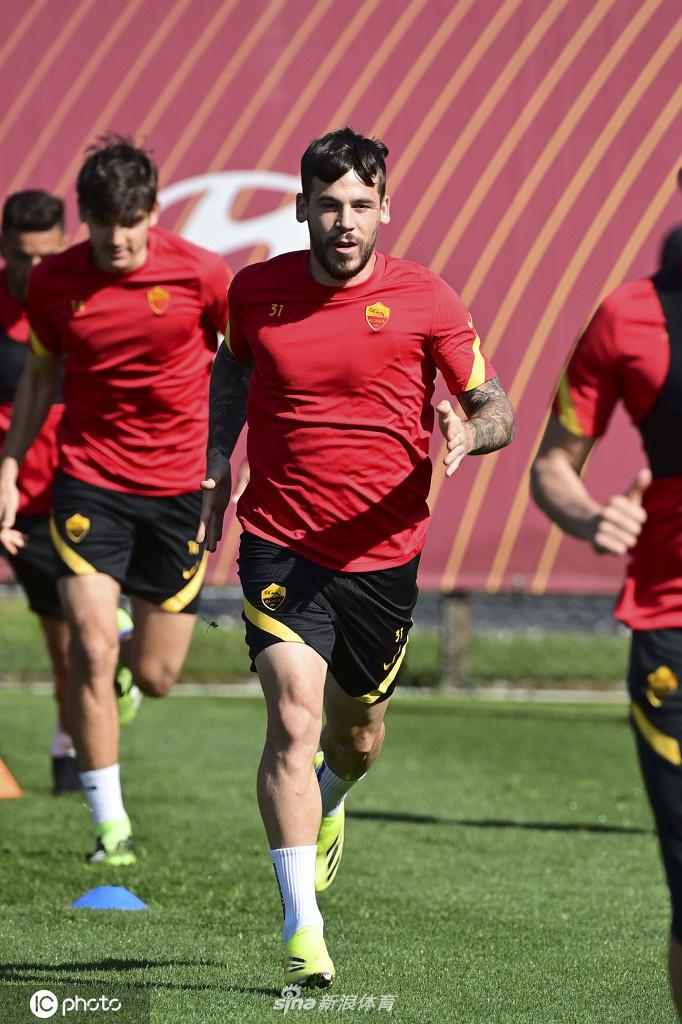 两名罗马中场球员在训练中进行激烈拼抢，其中一人飞身铲断，带起一片草屑，另一人则试图护球转身，肌肉紧绷，充满了力量的对决感。