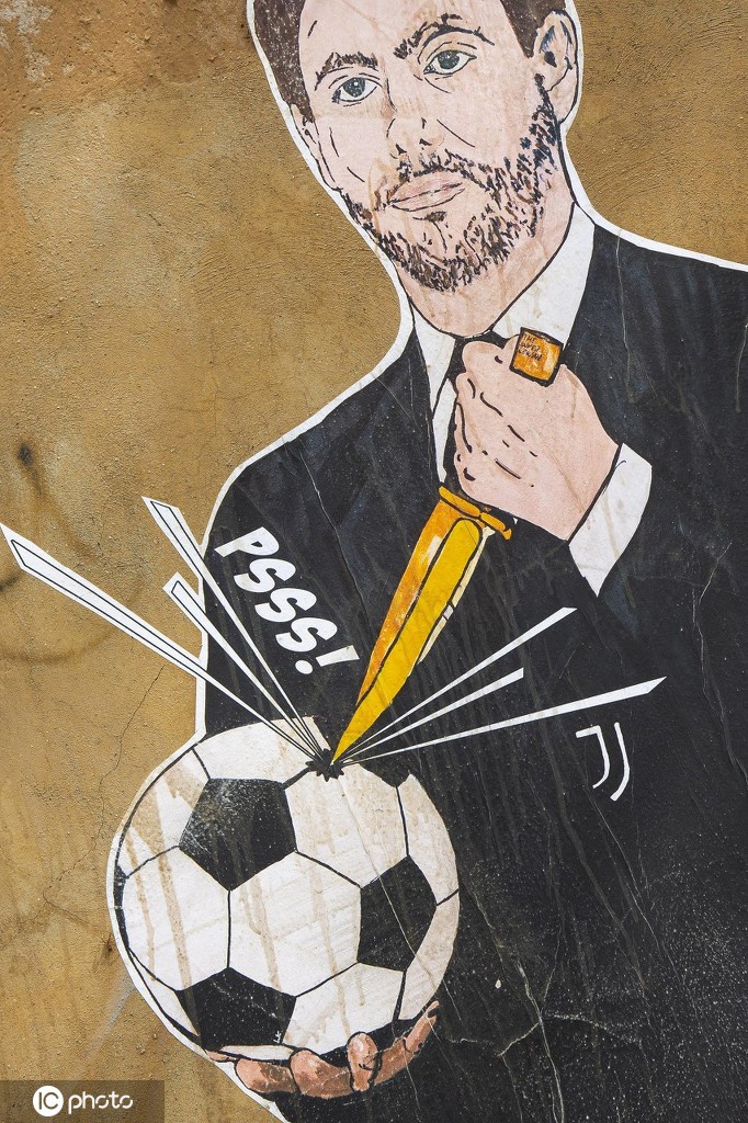 从低角度仰拍，壁画中的阿涅利显得异常高大，他手中的刀几乎要刺出画面，而下方恰好有一位戴着口罩的市民走过，这种垂直的构图让压迫感与反抗的渺小感形成了强烈的视觉冲击。