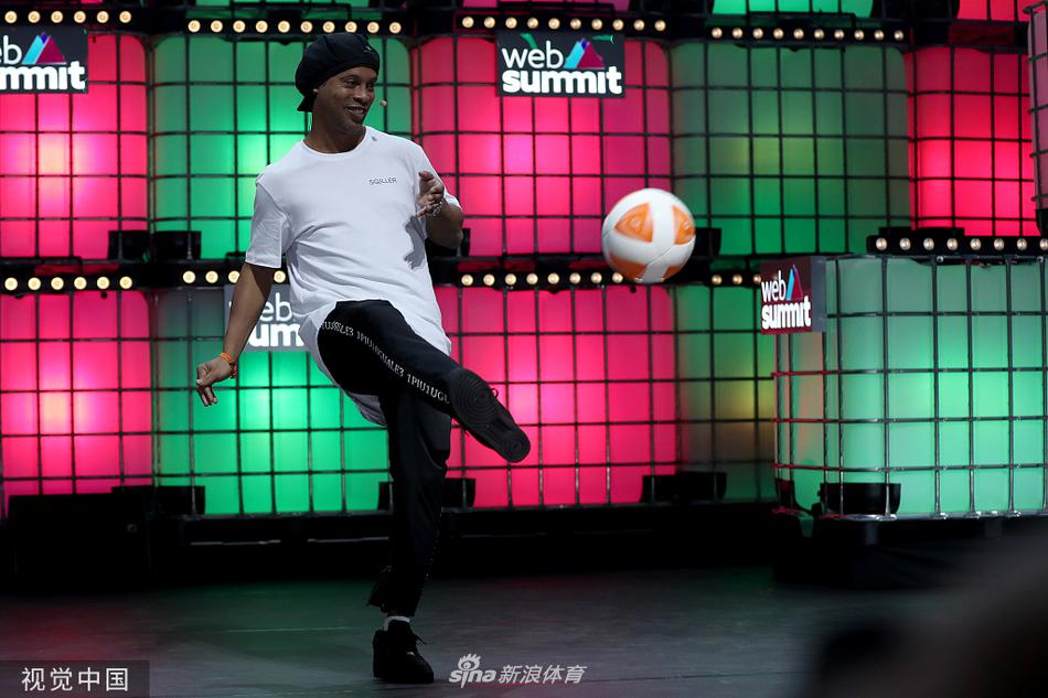 里斯本网络峰会现场人潮涌动，罗纳尔迪尼奥在安保人员陪同下穿过走廊，身旁的参会者纷纷举起手机记录这一刻