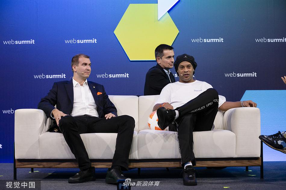 罗纳尔迪尼奥在峰会展厅内与一位身穿传统巴西黄衫的粉丝自拍合影，两人笑容灿烂，背景是科技公司的展台