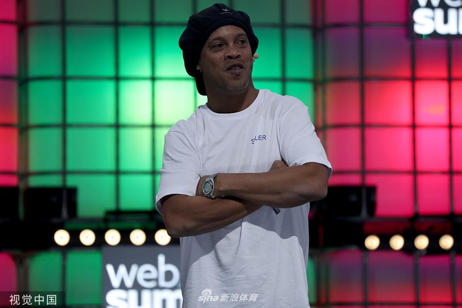 近景镜头捕捉罗纳尔迪尼奥在峰会上专注倾听的神态，胸前挂着参会证，周围是模糊的蓝色灯光与人群