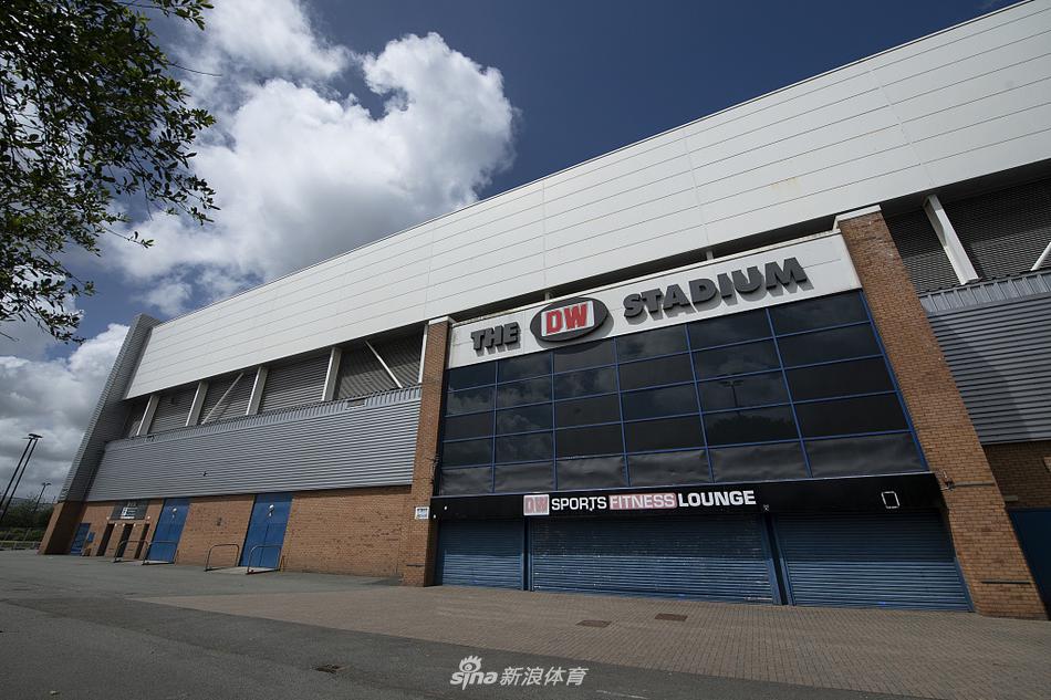 从高空俯瞰夏日的DW球场，四角敞开的看台结构尽收眼底，巨大的钢结构桁架在阳光下投下利落的阴影，仿佛一位静静守护着绿茵场的钢铁巨人。