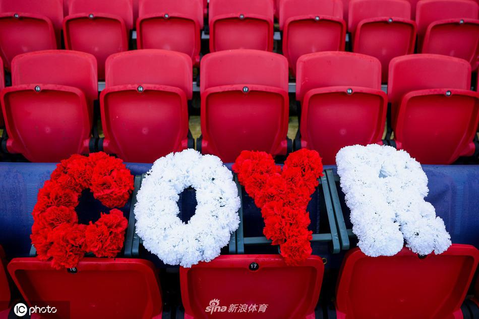 多束鲜花被整齐地放置在蓝色座椅上，花瓣上似乎还带着清晨的露珠。周围的座椅空无一人，但这份无声的集体守候，让整个空旷的看台都充满了人性的温度。