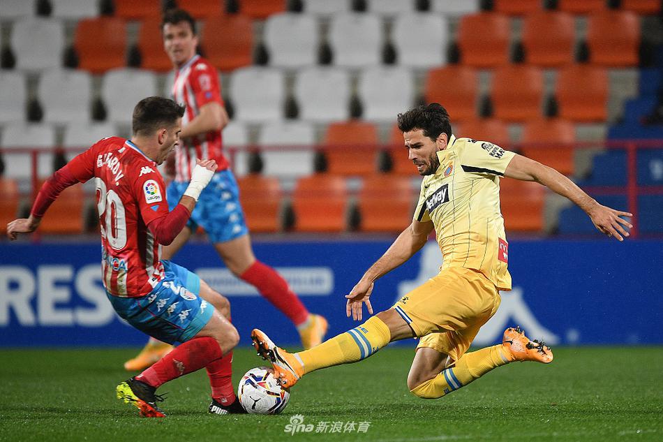 德托马斯在对方禁区内背身接应，面对两名卢戈防守球员的贴身夹防，他张开手臂努力保持平衡，眼神专注地寻找着传给队友的空当