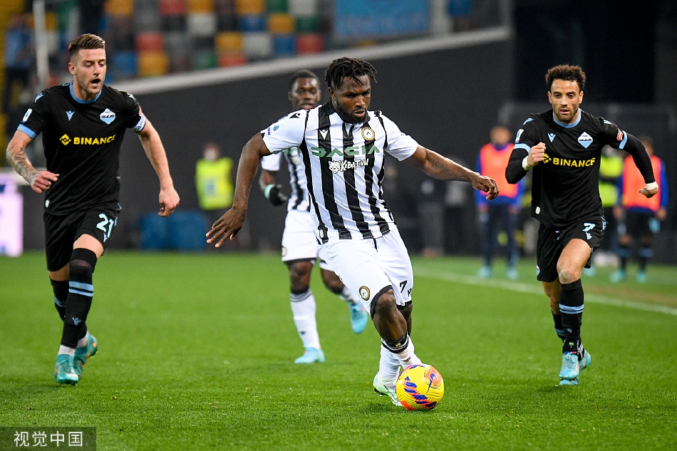 拉齐奥球员围绕主裁判激烈申诉，肢体语言丰富，而乌迪内斯球员则在一旁冷静观察，紧张的比赛氛围弥漫全场。