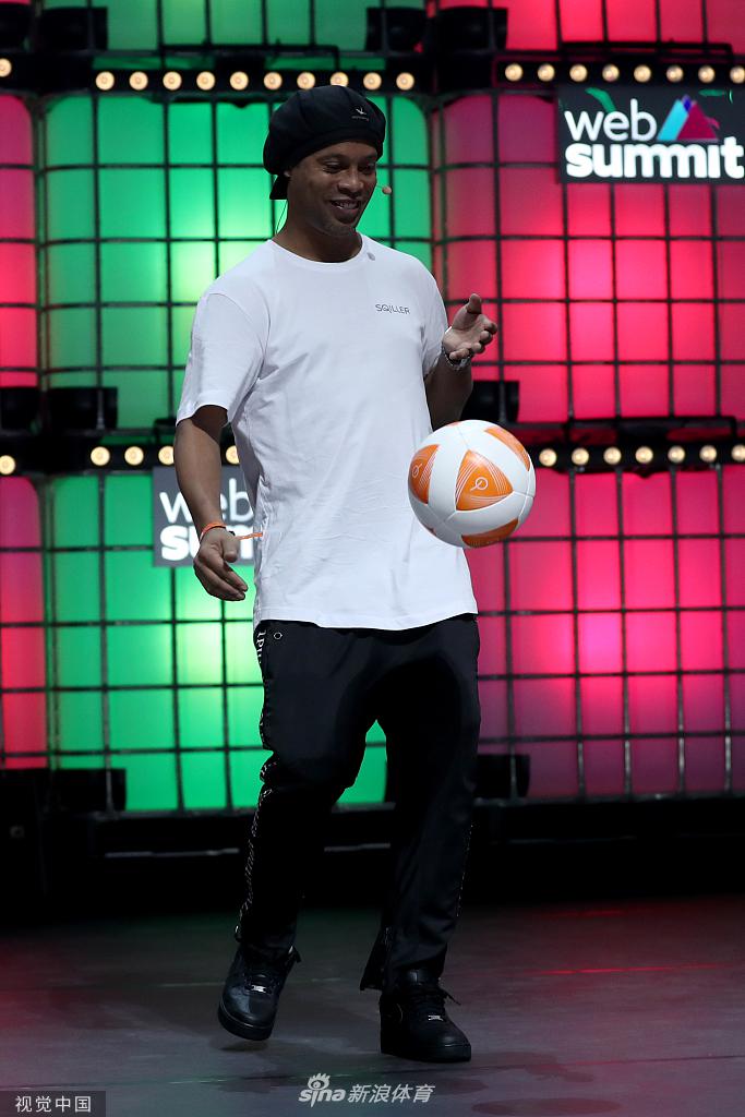 罗纳尔迪尼奥现身里斯本网络峰会，面带经典微笑向人群挥手，背景是峰会巨大的科技标识