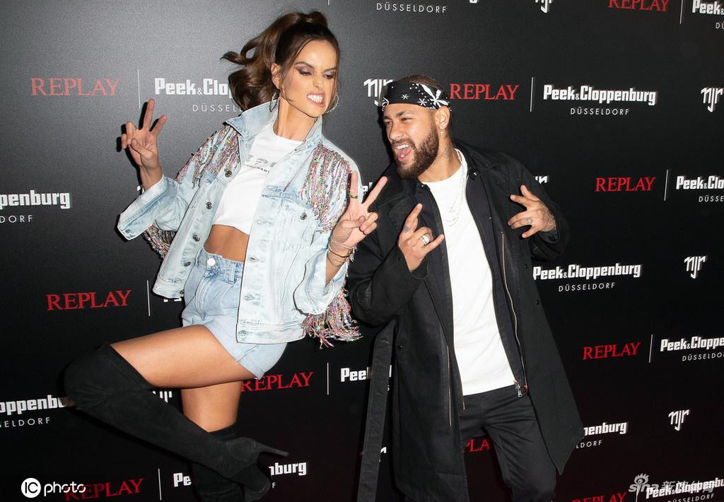 伊莎贝尔·歌勒在活动上穿着流苏牛仔短裤和白色印花短上衣，与台上的表演者互动，脸上洋溢着灿烂的笑容，氛围轻松愉快。