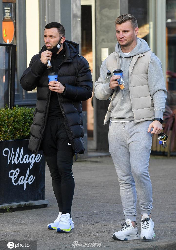 菲尔·巴德斯利身着深色羽绒服，与同样穿着休闲的兄弟并肩走在柴郡街头，他手中握着一杯外带咖啡，脸上带着轻松的笑容，仿佛正在谈论着什么家庭趣事。