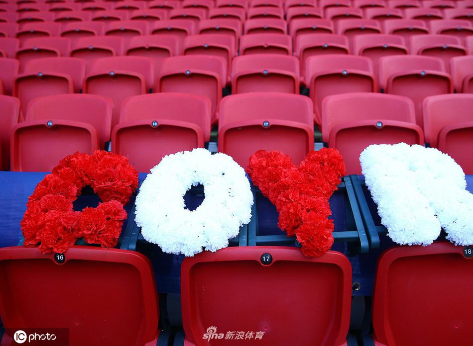 从稍远处看去，那片被鲜花点缀的看台格外醒目。阳光洒在座椅和花束上，形成一片温暖的光晕。这不仅仅是一个物理空间的装饰，更是球迷群体集体记忆和情感的具象化呈现。