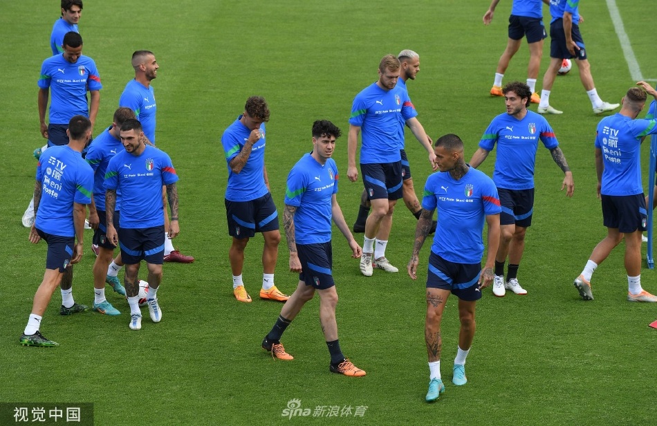 意大利全队围成一圈进行战术部署，主教练曼奇尼站在中心，用手势激昂地讲解着跑位路线，队员们神情专注，阳光将他们的身影拉长，构成一幅为共同目标而凝聚的动人画面。