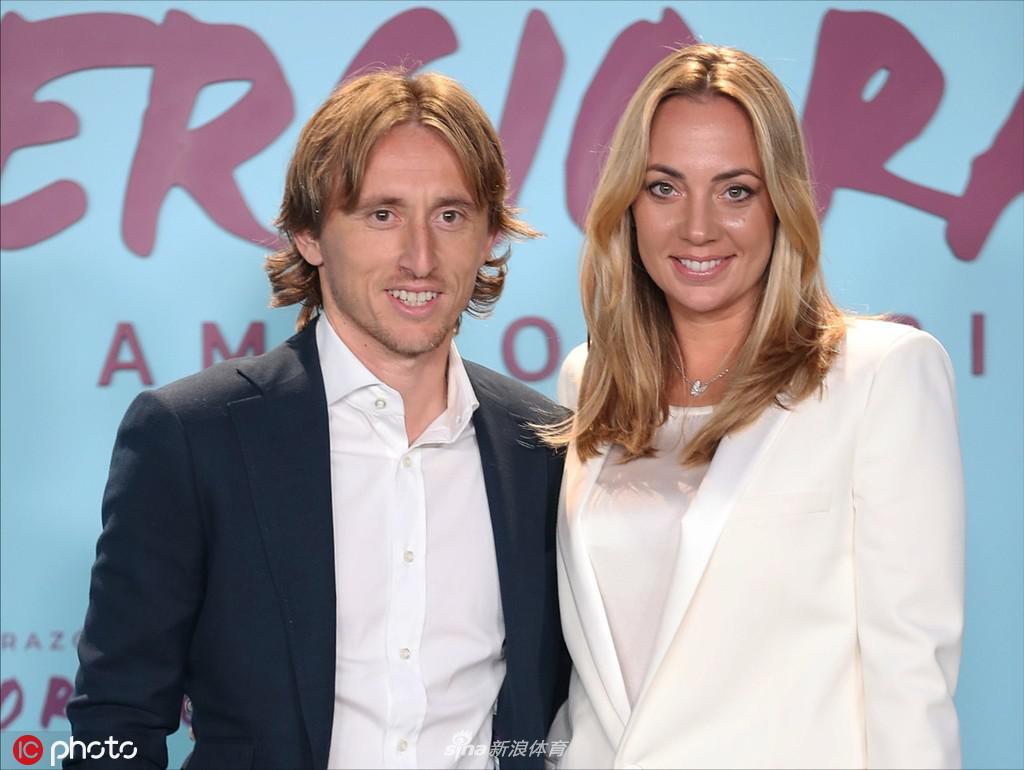 莫德里奇与妻子博斯尼奇十指紧扣踏上红毯，他身着剪裁得体的深色西装，笑容温暖，身旁的妻子一袭亮片长裙优雅动人，两人相视而笑的瞬间，仿佛让马德里的夜色都温柔了几分。