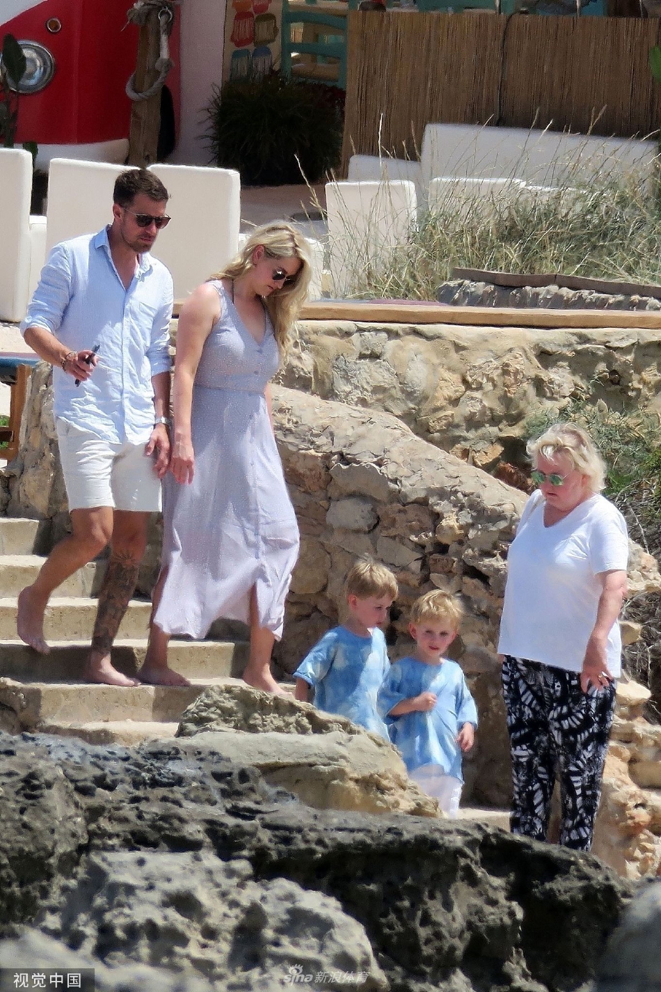 拉姆塞俯身与长子分享航海趣事，小男孩专注聆听父亲的话语，两人侧脸轮廓在夕阳余晖中勾勒出温馨的剪影