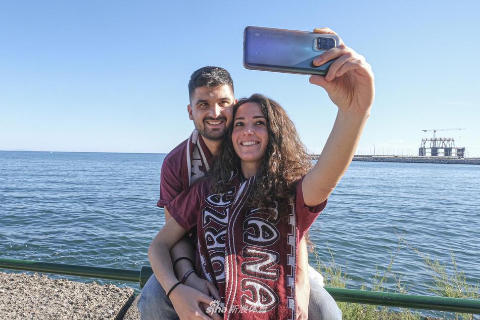  夜色降临，市中心的一条狭窄小巷里，狂欢的热度丝毫未减。几名年轻人手搭着肩膀，组成人浪，对着镜头释放着无尽的喜悦，背景中满是挂在窗外和阳台上庆祝升级的红白色旗帜和横幅。