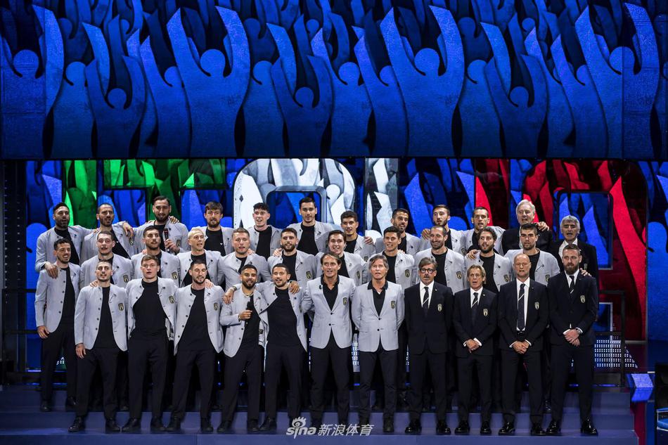 意大利队球星集体亮相舞台，深色西装笔挺，队伍中因莫比莱与若日尼奥正微笑注视镜头，背景是绚丽的演播厅灯光