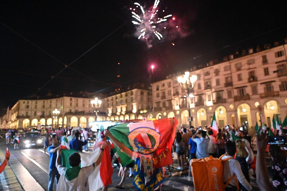 几名球迷站在一辆披着意大利国旗的敞篷汽车引擎盖上，他们拉着一条写着“GRAZIE AZZURRI”（谢谢你们，蓝衣军团）的横幅，对着镜头激动地挥舞着拳头。