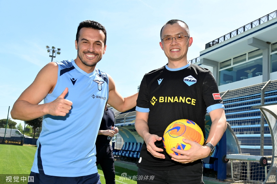 赵长鹏与拉齐奥队的主教练亲切交谈，两人站在训练场边，背景是正在进行热身活动的球员