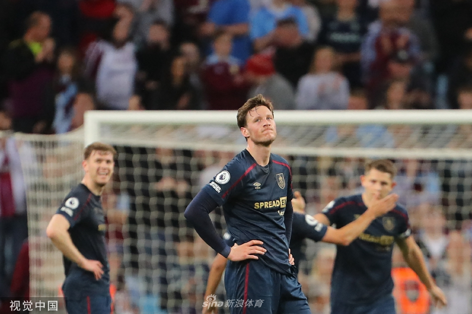 维拉公园球场全景，夕阳余晖笼罩着绿茵场，两队球员正在激烈拼抢，看台上座无虚席，气氛紧张而热烈。