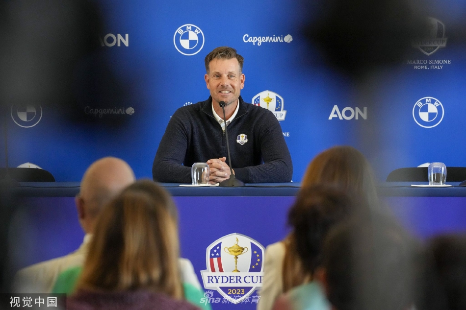 斯滕森与一位女士共同举起一座较小的纪念奖杯，脸上露出礼节性的笑容，台下观众席模糊，焦点集中于台上的互动。